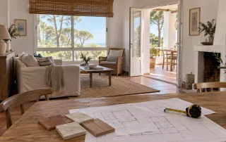 Interior de vivienda costera con planos y muestras de materiales para planificar una reforma; imagen conceptual generada con IA.